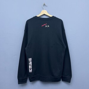 May include: A black long-sleeve crewneck sweatshirt featuring a red Andy Warhol signature and white double X graphic on the upper chest. A vertical strip of black and white photographic film-style images is printed on the lower right side.