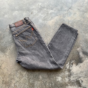 May include: A pair of faded black denim jeans. The jeans have a classic five-pocket design, with a brown leather patch on the back waistband and a red tag on the back pocket. The stitching is a contrasting tan color.