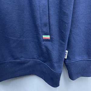 Puede incluir: Sudadera azul marino con un peque&ntilde;o bolsillo y un detalle de rayas tricolores en verde, blanco y rojo. El logotipo de la marca es visible en la parte inferior derecha. La sudadera es de un material suave.
