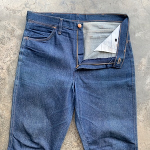 K&ouml;nnte beinhalten: Dunkelblaue Jeans aus Denim mit Knopfverschluss und Rei&szlig;verschluss. Die Jeans haben ein klassisches F&uuml;nf-Taschen-Design mit kupferfarbenen Nieten und N&auml;hten. Die Jeans sind aufgekn&ouml;pft und ge&ouml;ffnet und zeigen das Innenfutter.