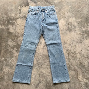 K&ouml;nnte beinhalten: Hellblaue Jeans aus Denim mit klassischem F&uuml;nf-Taschen-Design. Die Jeans haben eine gerade Beinpassform und bestehen aus verwaschenem Denim-Material. Die Jeans liegen flach auf einer Betonoberfl&auml;che.