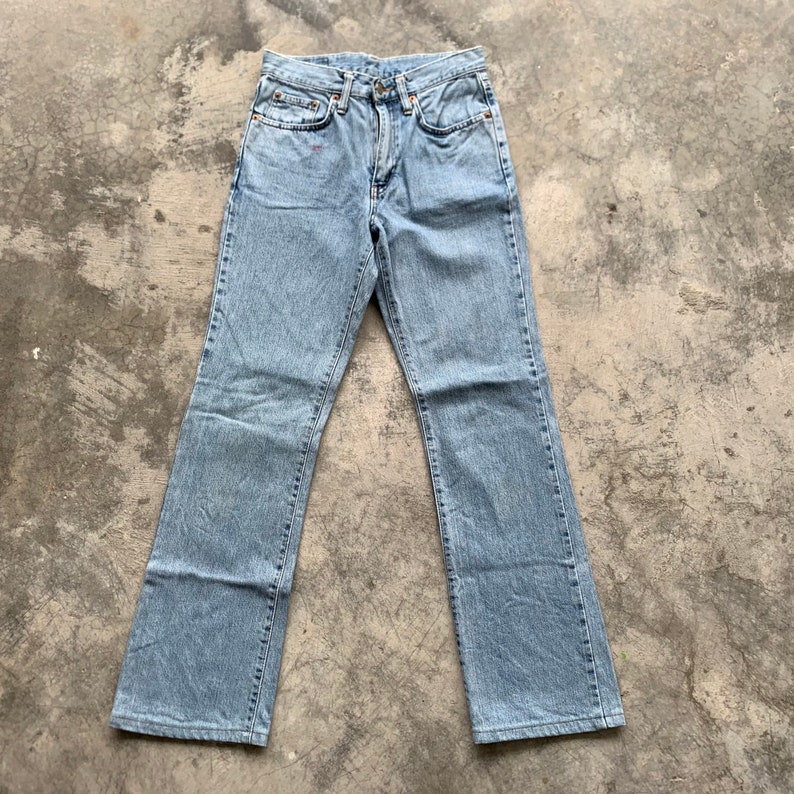 K&ouml;nnte beinhalten: Hellblaue Jeans aus Denim mit klassischem F&uuml;nf-Taschen-Design. Die Jeans haben eine gerade Beinpassform und bestehen aus verwaschenem Denim-Material. Die Jeans liegen flach auf einer Betonoberfl&auml;che.