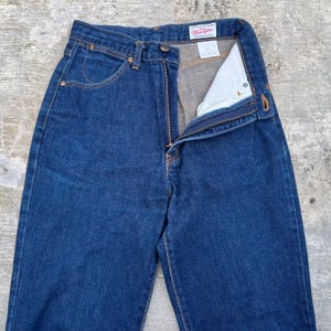 K&ouml;nnte beinhalten: Dunkelblaue Jeans aus Denim mit Rei&szlig;verschluss und Knopfverschluss. Die Jeans haben ein klassisches F&uuml;nf-Taschen-Design und eine gerade Beinpassform. Der Markenname "Wrangler" ist auf einem Etikett im Bund sichtbar.
