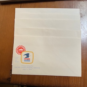 May include: A white envelope with a red and gold "First Day of Issue" stamp featuring a horse and rider. The envelope also has a blue and gold "U.S. Mail" logo and the text "Inaugurating the United States Postal Service July 1, 1971."