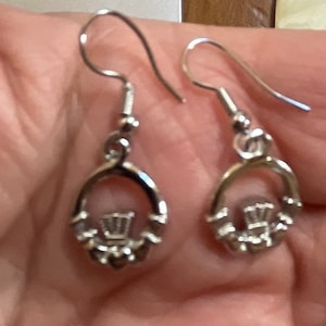 May include: A pair of silver dangle earrings featuring a Celtic knot design with a crown in the center.