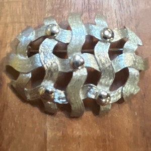 May include: A silver-toned brooch with a woven design and five round, silver-toned accents.