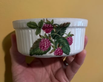 May include: A white ceramic ramekin with a ribbed exterior and a decorative raspberry design. The design features green leaves and clusters of pink raspberries. The ramekin is round and appears to be new.