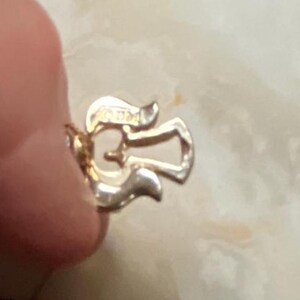 Pode incluir: Close-up de um fecho de metal dourado com um design decorativo. O fecho tem a forma de uma asa de anjo estilizada.