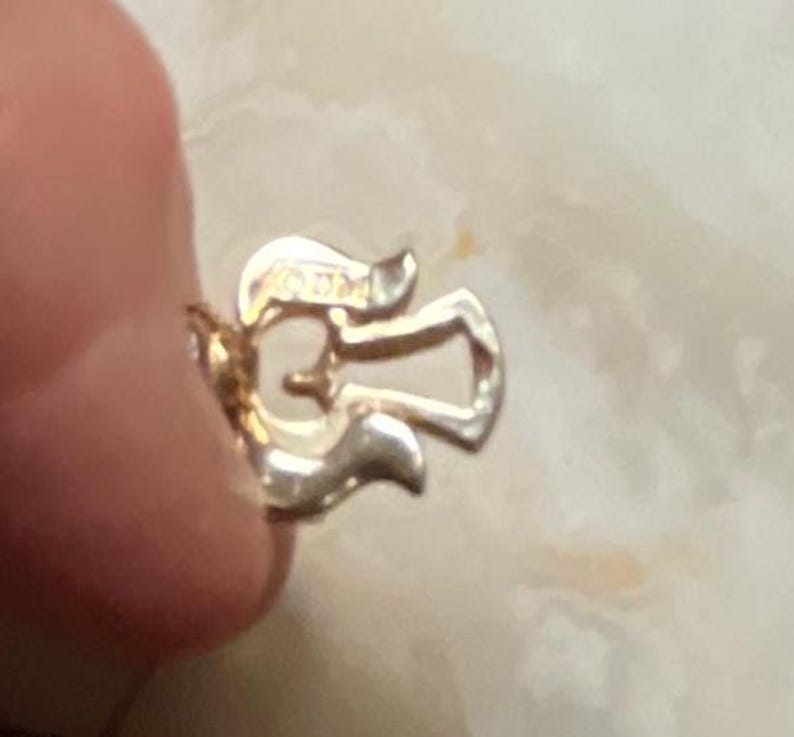 Pode incluir: Close-up de um fecho de metal dourado com um design decorativo. O fecho tem a forma de uma asa de anjo estilizada.
