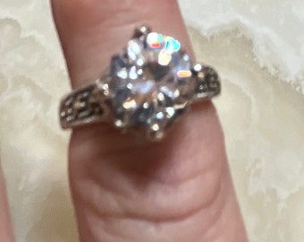 May include: A silver ring with a large, clear, round gemstone. The ring has a detailed, intricate design.