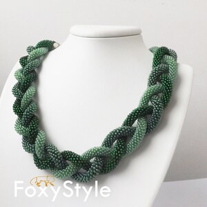 May include: A green beaded necklace with a gradient of shades from light to dark green. The necklace is made of small, round beads and is twisted into a rope-like design.