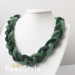 May include: A green beaded necklace with a gradient of shades from light to dark green. The necklace is made of small, round beads and is twisted into a rope-like design.