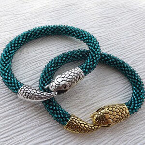 Puede incluir: Dos pulseras de serpiente de cuentas azul turquesa con cierres de cabeza de serpiente plateados y dorados.