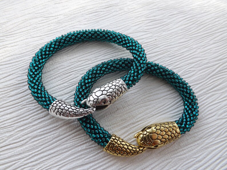 Puede incluir: Dos pulseras de serpiente de cuentas azul turquesa con cierres de cabeza de serpiente plateados y dorados.