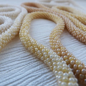 Puede incluir: Un conjunto de cuatro collares de cuentas en tonos de blanco, crema y beige. Los collares est&aacute;n hechos de peque&ntilde;as cuentas redondas y est&aacute;n dispuestos en un patr&oacute;n degradado, con el color m&aacute;s claro en la parte superior y el color m&aacute;s oscuro en la parte inferior.
