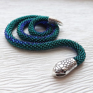 May include: A beaded snake necklace with a silver snake head charm. The necklace is made with green and blue beads and is coiled into a snake shape.