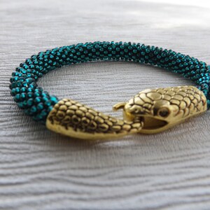 Puede incluir: Un brazalete de cuentas azul turquesa con un cierre de cabeza de serpiente dorada.