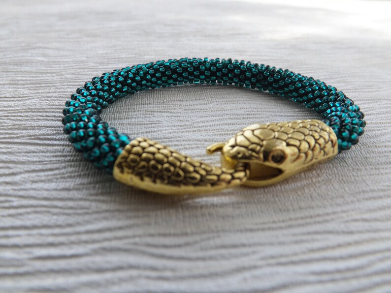 Puede incluir: Un brazalete de cuentas azul turquesa con un cierre de cabeza de serpiente dorada.