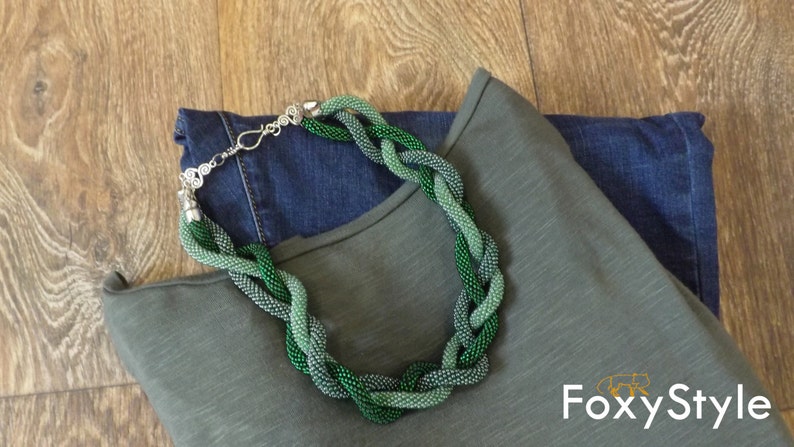 May include: A green and blue beaded necklace on a folded green and blue shirt with the text "FoxyStyle" on the bottom right corner.
