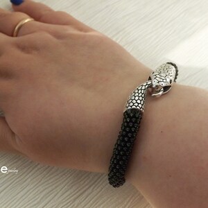 Puede incluir: Un brazalete negro de cuentas con un cierre de cabeza de serpiente plateado. El brazalete est&aacute; en la mu&ntilde;eca de una persona.