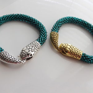 Puede incluir: Dos pulseras de serpiente de cuentas verde azulado con cierres de cabeza de serpiente plateados y dorados.
