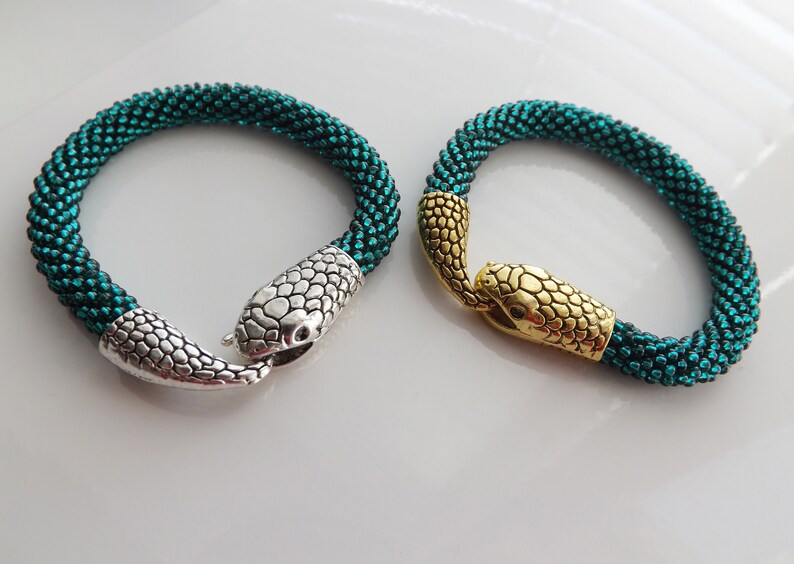 Puede incluir: Dos pulseras de serpiente de cuentas verde azulado con cierres de cabeza de serpiente plateados y dorados.