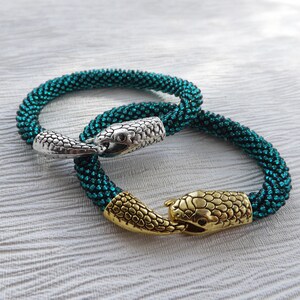 Puede incluir: Dos pulseras de cuentas con cierres de cabeza de serpiente. Una pulsera es de color turquesa y la otra es de color turquesa m&aacute;s oscuro.