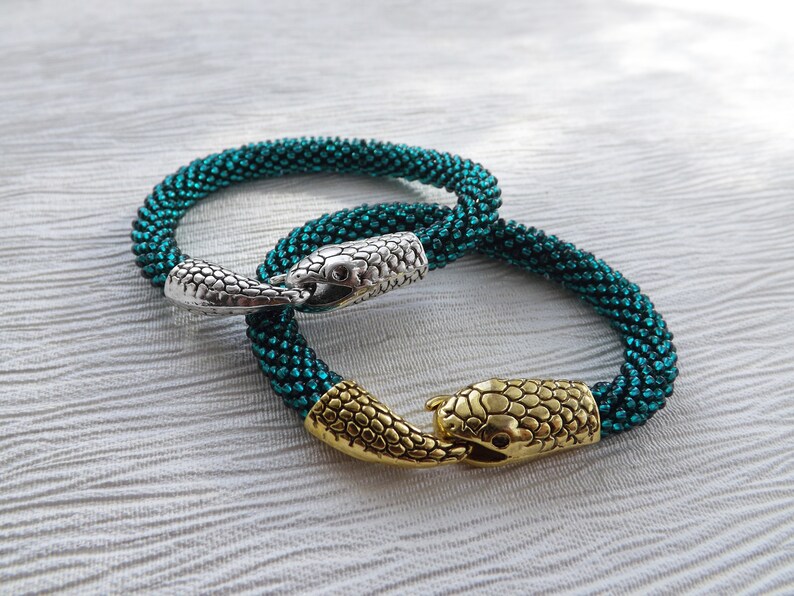 Puede incluir: Dos pulseras de cuentas con cierres de cabeza de serpiente. Una pulsera es de color turquesa y la otra es de color turquesa m&aacute;s oscuro.