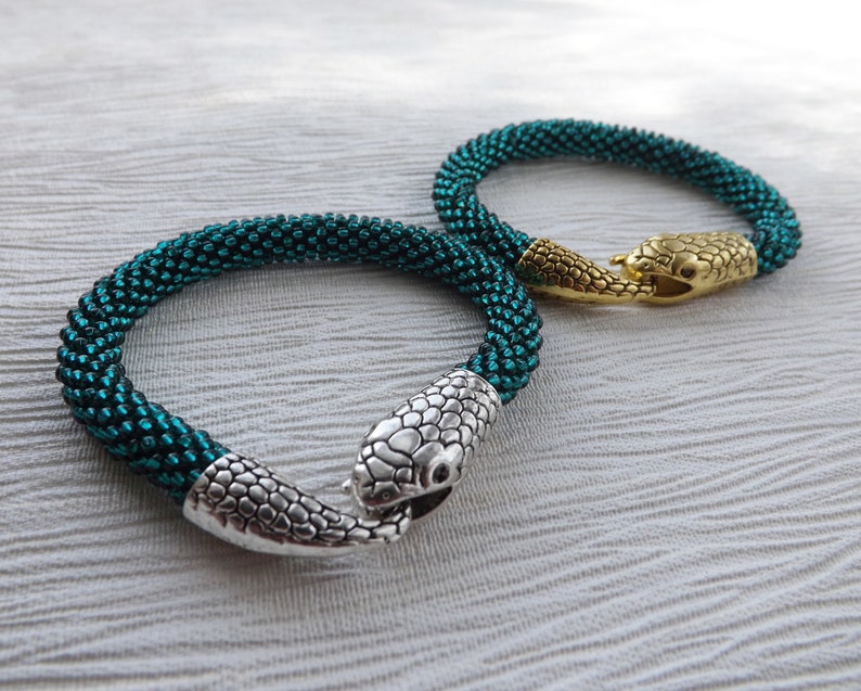 Puede incluir: Dos pulseras de serpiente de cuentas con cierres de cabeza de serpiente plateados y dorados. Las pulseras son de color azul verdoso y est&aacute;n hechas de cuentas peque&ntilde;as.