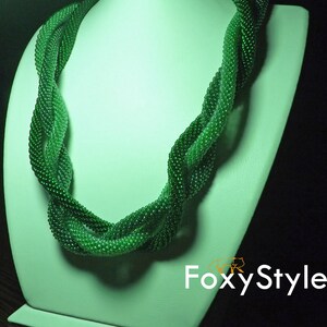 May include: A green beaded necklace with a twisted design. The necklace is displayed on a white mannequin bust.