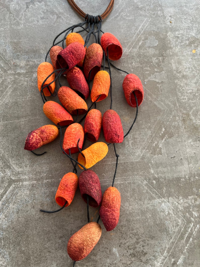 May include: A necklace made of natural materials, featuring a cluster of orange, red, and yellow pods hanging from a brown leather cord.