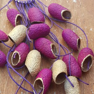 May include: A collection of purple and gold silk cocoons, tied together with a purple cord. The cocoons are arranged in a fan shape, with the gold cocoons at the bottom and the purple cocoons at the top.