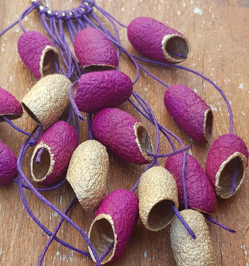 May include: A collection of purple and gold silk cocoons, tied together with a purple cord. The cocoons are arranged in a fan shape, with the gold cocoons at the bottom and the purple cocoons at the top.