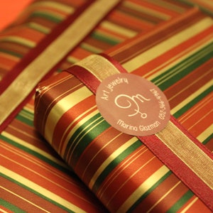 May include: Two red, gold, and green striped gift boxes with a red ribbon and a round, pink label that says "Art Jewelry, M, Marina Glazman, 052-546-2550".
