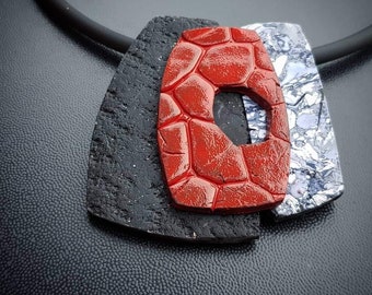May include: A black, red, and silver necklace with three geometric pendant shapes. The red pendant has a textured surface.