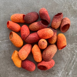 May include: A collection of 17 orange, red, and brown silk cocoons. The cocoons are arranged in a pile on a gray surface.