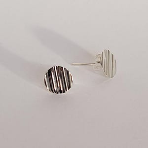 Op de afbeelding: Een paar zilveren oorbel studs met een geribbeld, rond ontwerp.