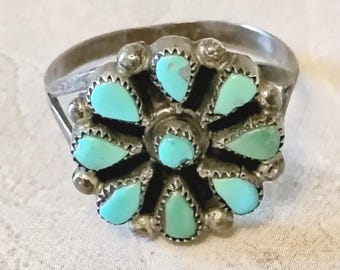 May include: A silver ring featuring a floral design with turquoise teardrop-shaped stones. The ring has a detailed setting with small silver beads around each turquoise stone. The ring's band is a simple, rounded design.