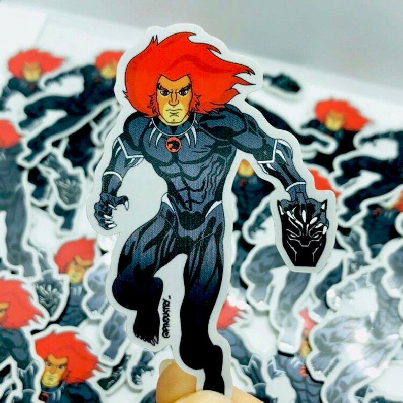 May include: A black and white sticker of Lion-O from ThunderCats. He is wearing a black suit with a red chest piece and a black panther mask. The sticker is on a white background.