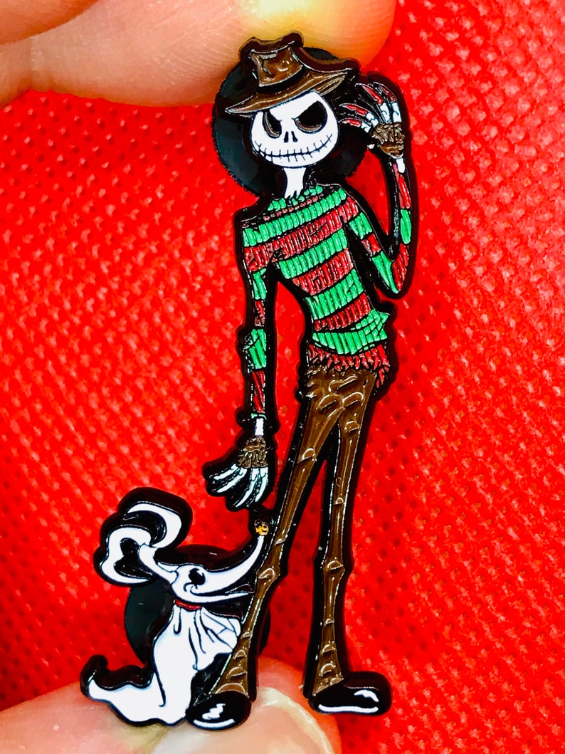 May include: A black and white enamel pin featuring a cartoon version of Jack Skellington from The Nightmare Before Christmas dressed as Freddy Krueger from the Nightmare on Elm Street franchise.  The pin also features a small, white, cartoon dog.