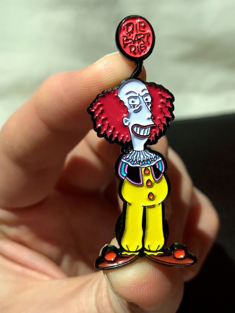 May include: A red and black enamel pin featuring a cartoon character with red hair, a yellow jumpsuit, and a red balloon that says "Die Bart Die".