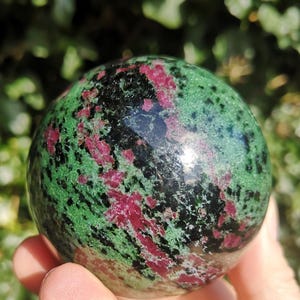 May include: Green, black, and pink gemstone sphere. The sphere is polished and has a smooth surface.