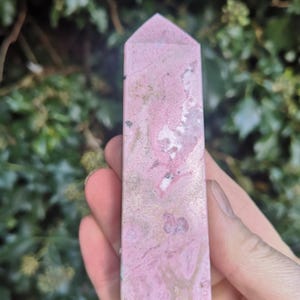 May include: A polished pink and white crystal point with a pointed tip. The crystal has a marbled appearance with swirls of pink, white, and gold.