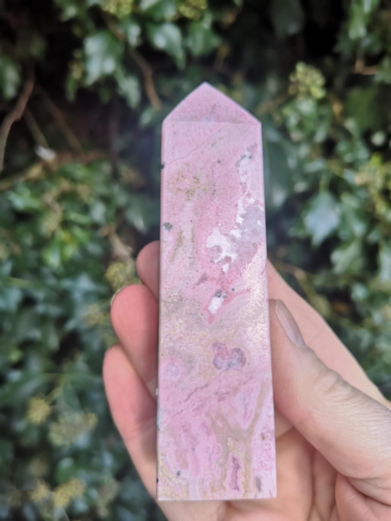 May include: A polished pink and white crystal point with a pointed tip. The crystal has a marbled appearance with swirls of pink, white, and gold.