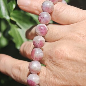 May include: A beaded bracelet featuring smooth, spherical stones with a marbled appearance in shades of deep pink, magenta, and translucent white. The beads are strung together in a single row, showcasing natural color variations and polished surfaces.