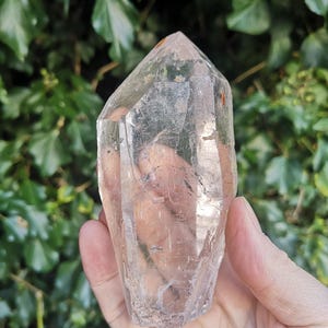 May include: A clear quartz crystal point with a natural, raw finish. The crystal is held in a hand, showcasing its size and shape.