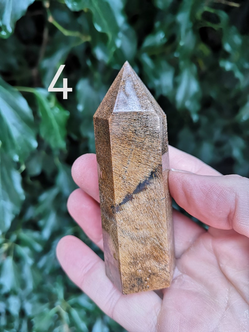 Puede incluir: Una punta de cristal marr&oacute;n y blanco con una parte superior puntiaguda y una superficie lisa y pulida. El cristal mide aproximadamente 10 cm de alto y se sostiene en una mano.
