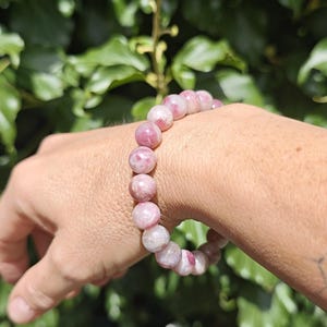 May include: A beaded bracelet featuring round, polished stones in varying shades of pink, magenta, and white. The beads are strung together in a continuous circular pattern, displaying natural marbling and translucent textures throughout each individual stone.