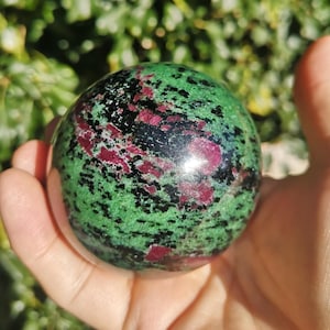 May include: Green, black, and pink gemstone sphere. The sphere is polished and has a smooth surface.