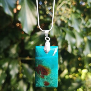 Pu&ograve; includere: Una collana con pendente rettangolare con catena d'argento. Il pendente &egrave; un vivace mix di turchese e verde acqua con inclusioni rossastre. Il pendente &egrave; lungo circa 3,8 cm.
